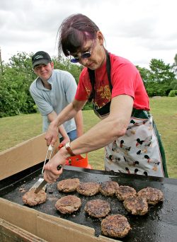 Marjorie cooking our big, thick, delicious Scottish | Kobe hamburgers at the Powick Fete, with Andy looking on in amusement. The wind kept blowing out our industrial-strengh barbeque, so we had to construct a barrier of cardboard boxes.